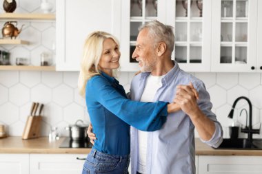 Portrait Of Loving Senior Couple Dancing Together In Kitchen Interior, Happy Romantic Elderly Spouses Having Fun, Holding Hands And Smiling To Each Other, Enjoying Spending Time At Home, Closeup Shot