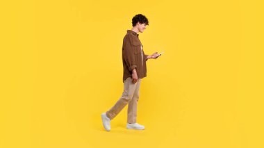 Mobil uygulama. Akıllı telefon kullanan genç bir adamın sarı arka planda yürürken sosyal medya yayını ve mesajlaşması, stüdyo çekimi. Telefon web sörfü ve panorama yapan bir sürü adam.