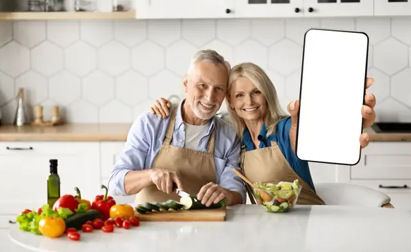 Delivery App. Happy Senior Couple Showing Big Blank Smartphone While Cooking In Kitchen At Home, Smiling Elderly Spouses Recommending New Mobile Application Or Website, Collage, Mockup