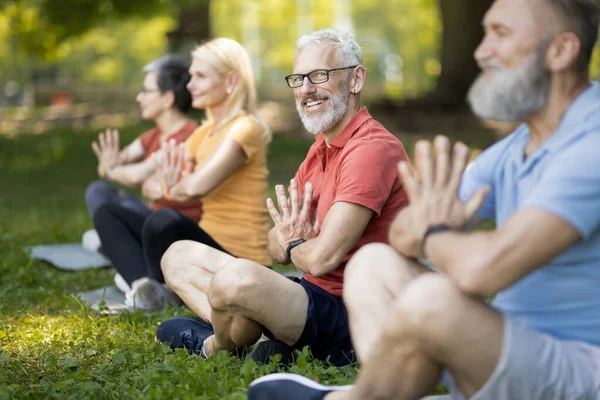 Yakışıklı son sınıf öğrencisi yoga sınıfının portresi arkadaşlarıyla parkta meditasyon yapan, Lotus pozisyonunda oturan ve kameraya gülümseyen mutlu bir centilmen.