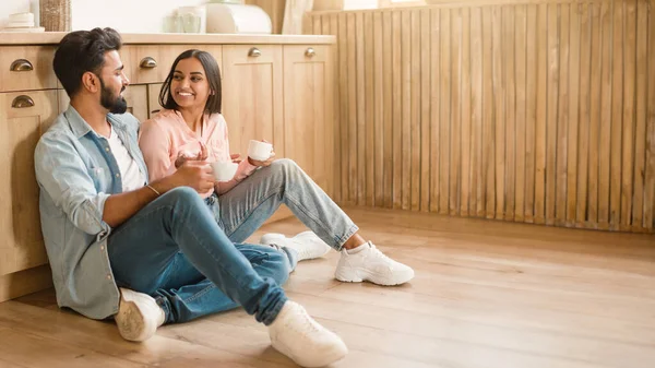 ハッピー若いインドの配偶者とコーヒーを飲んで話すカップ キッチンインテリアの床に座って 無料のスペースでパノラマ 自宅で一緒にリラックスするヒンドゥーのカップル — ストック写真