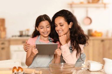 İnternetteki Tarifler. Modern mutfakta hamur işi pişirirken Dijital Tablet kullanan Mutlu Arap Anne ve Kızı. Çocuk Web Sörfü Lezzetli Pasta Tarifi, Annesiyle Bilgisayar Aşçılığı