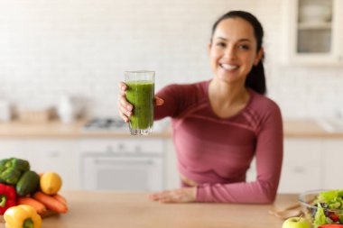 Sağlıklı Detox Diyet. Fitness Lady, evdeki modern mutfakta yeşil meyve suyu içmeyi, cam tutmayı ve kameraya el uzatmayı, zayıflamayı ve kilo vermenin tadını çıkarmayı teklif ediyor. Seçici Odaklanma