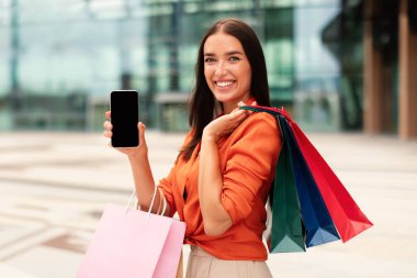 Alışveriş Başvurusu. Modern AVM 'nin yanında duran, dışarıda cep telefonu tutan, Mockup Holding için Boş Ekranlı Mutlu Müşteri Bayan Akıllı Telefonu Gösteriyor.