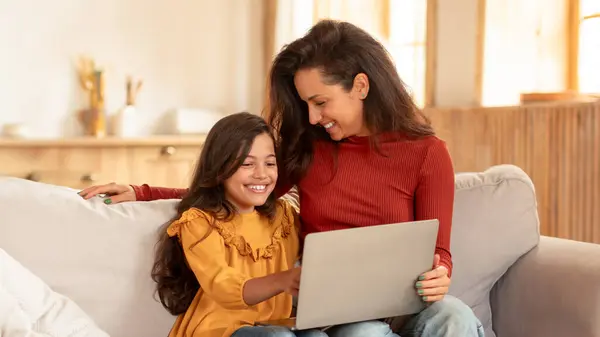 快乐的中东妈妈和女学生在现代客厅用笔记本电脑 在电脑前坐着 在网上浏览 周末在家里玩在线游戏 — 图库照片