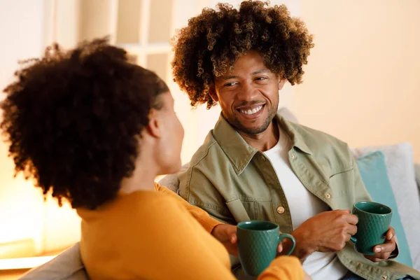 Coffee and Conversations. African American Young Spouses Bonding Over Hot Drink and Flirty Talks, Sitting With Coffee Cups And Smiling To Each Other At Home. Selective Focus