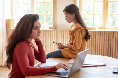 Genç Arap anne, dizüstü bilgisayarda çalışan kızını görmezden geliyor ve evde masada oturan mutlu olmayan kız internette sörf yaparken sıkılıyor. Ebeveyn ilgisizliği. Seçici Odaklanma