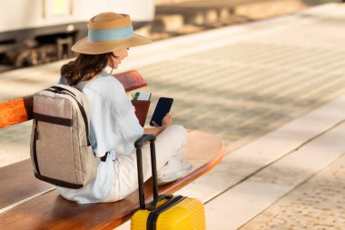 Çantalı gülen bin yıllık beyaz kadın havaalanında, tren istasyonunda sırt çantasıyla sohbet ediyor. Seyahat yaşam tarzı, seyahat günlüğü, online rezervasyon, tatil ve iş uygulaması