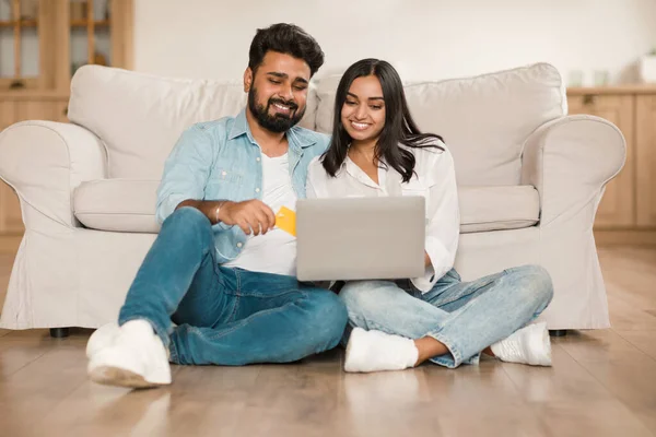 ハッピーヒンドゥーのカップルは 家庭からラップトップとクレジットカードでオンラインショッピング インドの配偶者は インターネット支払いを行う リビングルームの床に座って 無料のスペース — ストック写真