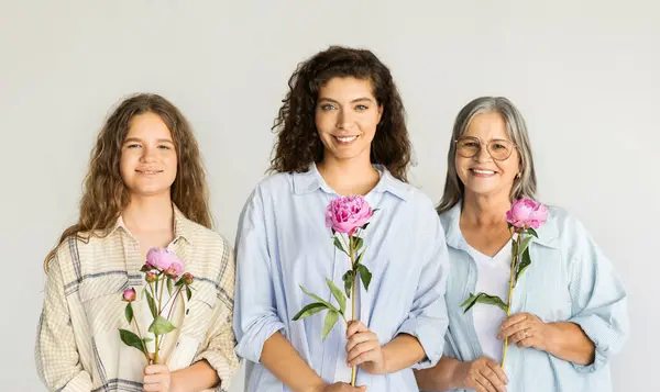 Happy caucasian diverse women in casual holding flowers, enjoy freshness, cleanliness on white wall background. Grandma, mom and daughter, parents relationships, ad and offer
