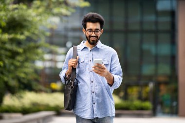 Bin yıllık olumlu Hintli girişimci adam sabahları ofise gidiyor, cep telefonunu sokakta kullanıyor, fotokopi çekiyor. Mutlu genç doğulu adam e-postaları kontrol ediyor, akıllı telefonları açık havada kaydırıyor.