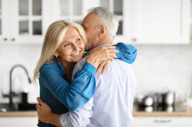 Mature Romance. Beautiful Senior Woman Tenderly Embracing Her Husband In Kitchen, Closeup Shot Of Loving Elderly Spouses Having Romantic Moments At Home, Enjoying Spending Time Together