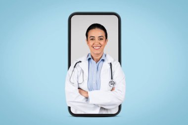 Beyaz üniformalı genç Brezilyalı kadın doktor steteskop ile poz veriyor ve kollarını katlayarak büyük bir cep telefonu ekranı, mavi arka plan, afiş. Tıbbi hizmetler kavramı