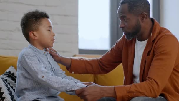 シンシアな親愛 アフリカ系アメリカ人の父親が彼の怒った息子に話しかけ 人生の瞬間を説明し 彼を落ち着かせ 家で一緒に座って サイドビュー — ストック動画