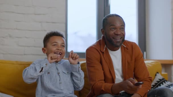ファミリースポーツファン エキサイティングな感情的なアフリカ系アメリカ人の父親と息子は テレビでサッカーの試合を見て お気に入りのチームをサポートし ゴールを楽しんで ショットを追跡し スローモーション — ストック動画