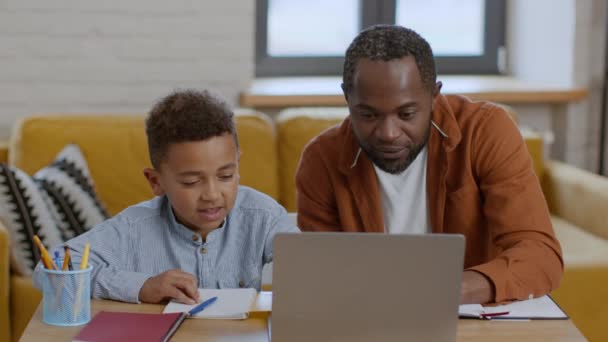 ポジティブなホームスクーリング かわいい小さな黒人の少年 彼のパパとオンラインで勉強 よくやった宿題を楽しんで お互いに微笑み 追跡ショット スローモーション — ストック動画
