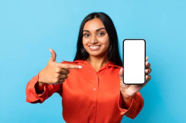 Harika bir uygulama. Cep telefonunu boş ekranla gösteren mutlu Hintli genç bayan, Mobil Aygıt Reklam Uygulaması 'nı işaret ediyor Mavi Stüdyo Arkaplanı' nın üzerinde duruyor. İletişim Teklifi. Model