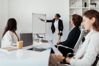 Profesyonel sunum. Siyahi iş kadını şirket toplantısında konuşma yapıyor, beyaz tahtaya işaret ediyor başlangıç stratejisini, ofis iç işlerini anlatıyor.