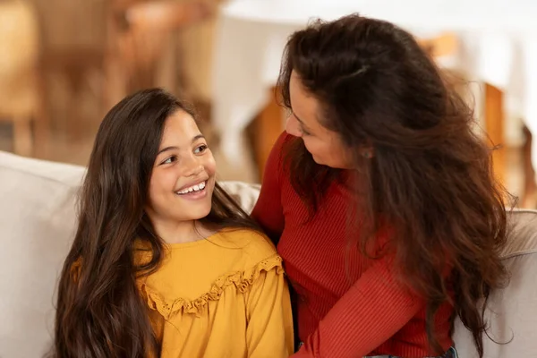 Mom And Daughter Bond. Portrait Of Happy Arabic Preteen Girl Smiling And Talking To Mommy, Enjoying Time Together On Living Room Sofa At Home. Family, Good Relationship With Mother. Selective Focus