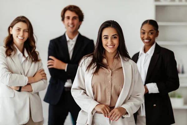 Leadership and entrepreneurship career. Positive young latin businesswoman leader standing in front of her multiracial employees, posing in light office interior
