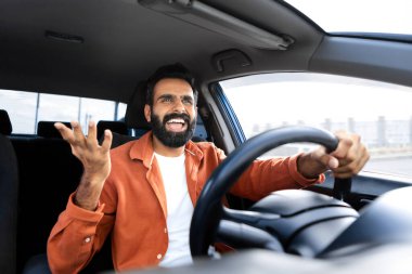 Şoför koltuğunda otururken bağıran ve direksiyonu modern otomobilin içinde tutan sinirli, agresif Hintli adam, hoşnutsuzluğunu ifade ederek riskli araba kullanıyor. Trafik sıkışıklığı sorunu, araba kazası riski