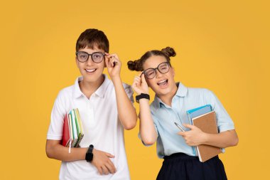 Gözlüklü Avrupalı ergen okul çocukları okulda eğleniyor, eğitimin tadını çıkarıyor, turuncu stüdyo arka planında yalnız kalıyorlar. Çalışma, bilgi, arkadaşlık ve çocukluk yaşam tarzı