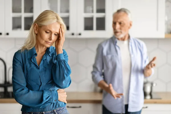 Portrait Of Upset Elderly Couple Arguing Together In Kitchen Interior, Senior Husband And Wife Having Domestic Conflicts, Suffering Relationship Crisis, Selective Focus On Crying Woman