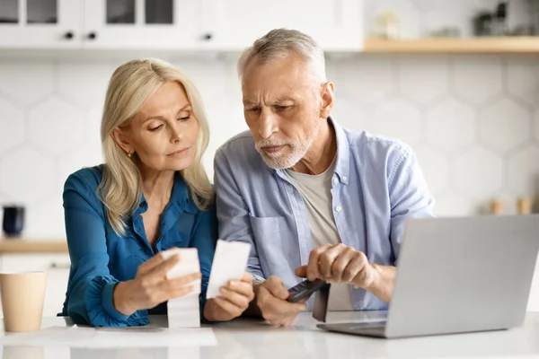 Senior couple in kitchen checking bills and using calculator, elderly husband and wife counting monthly expenses, planning family budget while spending time together at home, free space