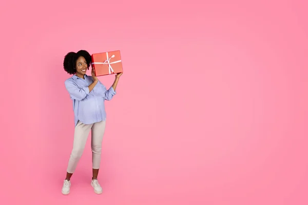 ポジティブな好奇心旺盛なミレニアルブラックレディーと大きな腹のリスニングボックス ピンクの背景に隔離されたギフト スタジオ プレゼントアイデア 誕生日おめでとう 生まれていない子供のパーティー — ストック写真