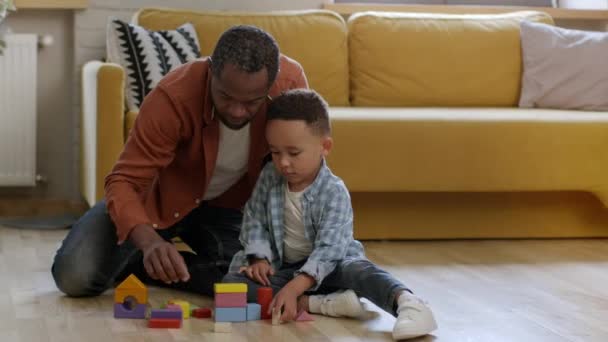 パターン放棄と子供の育成 愛するアフリカ系アメリカ人のパパは 彼のかわいい息子とカラフルなブロックを演奏し 家で床に一緒に城を建て ショットを追跡 スローモーション — ストック動画
