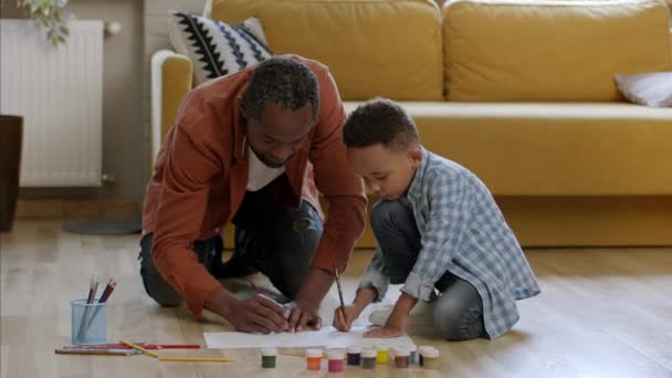 自宅でのクリエイティビティ開発 彼の父親と床に描いた集中した黒人の少年 一緒にアート写真を作成し ショットを追跡し スローモーション コピースペース — ストック動画