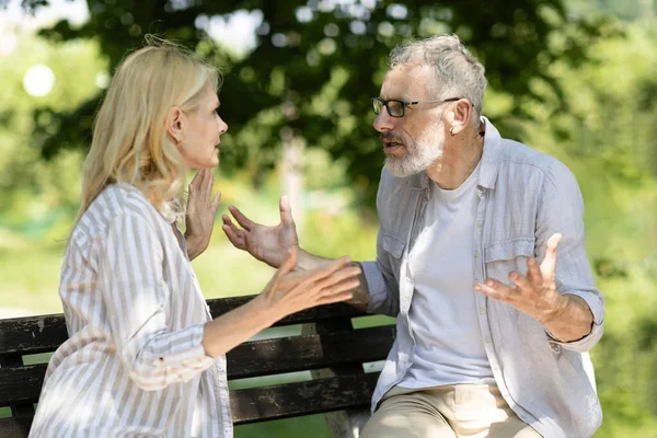 Portrait Of Mature Couple Arguing Outdoors While Sitting On Bench In Park, Senior Man And Woman Emotionally Quarrelling Outside, Suffering Relationship Crisis And Misunderstanding, Closeup