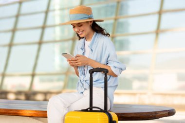 Bavullu, bin yıllık beyaz bir bayan havaalanında, tren istasyonunda akıllı telefondan sohbet ediyor. Seyahat yaşam tarzı, insan duyguları, uygulamalı online rezervasyon