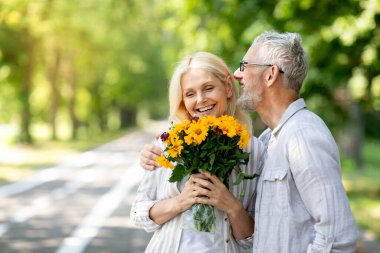 Son sınıf öğrencisi karısını Uluslararası Kadınlar Günü 'nde karşılıyor, çiçek buketi veriyor ve mutlu eşi kucaklıyor, romantik olgun çift güneşli parkta birlikte yürüyor, dışarıda eğleniyor.