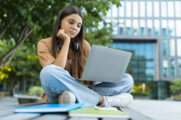 心烦意乱的女大学生一个人坐在公园的长椅上 拿着笔记本电脑 做作业 在项目或家庭作业上有困难 悲伤的女士感到孤独 空虚的空间 — 图库照片
