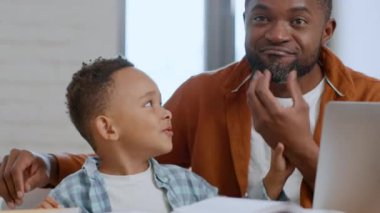 Baba ve oğul samimi bir sevgi. Şirin Afrikalı Amerikalı küçük çocuk babasıyla oynuyor, sakalını okşuyor ve evde gülüyor, portresini yakından çekiyor.