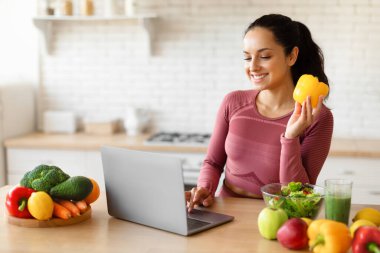 Spor Giyim 'de gülümseyen kadın, mutfakta yemek pişirirken, kilo verme reçeteleri ararken, yemek hazırlarken, beslenme ve diyet günlüğü okurken ya da web sitesinde biber tutarken, dizüstü bilgisayar kullanıyor.