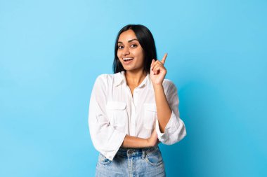 İlham ve yaratıcılık. Heyecanlı genç Hintli kadının portresi parmağını kaldırıyor, mavi stüdyo arka planında yaratıcı bir fikre sahip, kameraya gülümsüyor. Harika çözüm, eureka konsepti