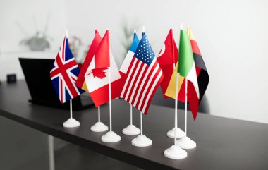 Uluslararası Konferans Toplantısı sırasında ofis masasında duran birçok farklı ülke bayrakları ve dizüstü bilgisayarı. İnsanlar yok, Nesneler. Yurtdışında Küresel Çevrimiçi İş ve Eğitim