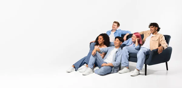 エキサイティングな多様な十代の友人がテレビを見て 白いスタジオの背景の上にソファーや床に座って コピースペース パノラマ バナーを見ています — ストック写真