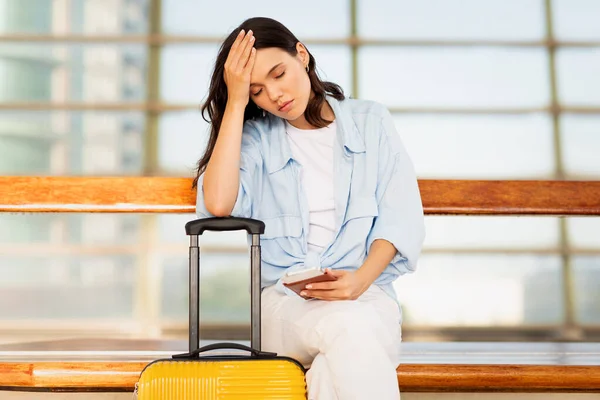 Despaired sad young caucasian lady with suitcase, smartphone and ticket, suffers from late for transport on train station or airport. Problems and stress, travel mistake and lifestyle