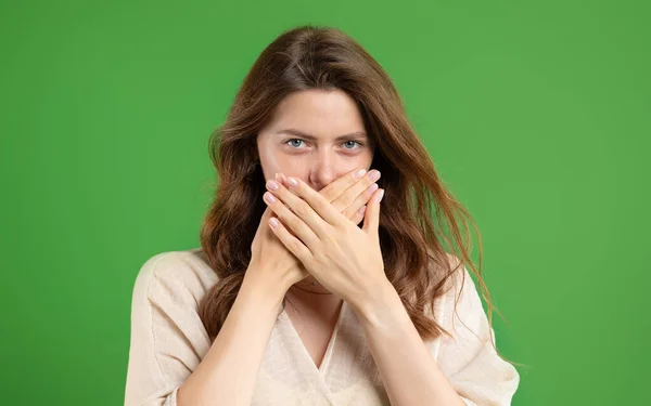 严肃的年轻的欧洲女人在随意地合上嘴与手 保守秘密 隔离在绿色工作室背景 惊奇和沉默 人类的情感 广告和提供 — 图库照片