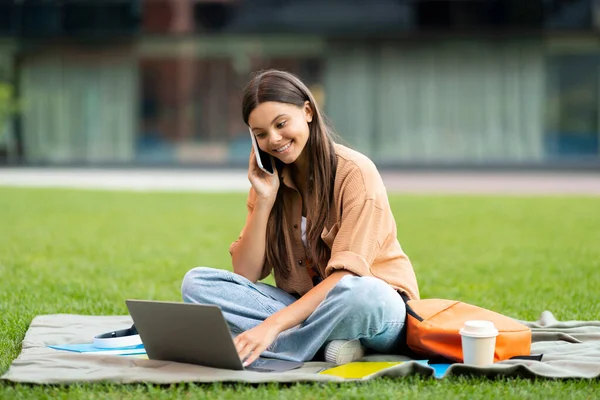 アルバイト 学生のためのフリーランス コンピュータのラップトップを使用してポジティブで美しい若い女性は 屋外の雇用主と電話で話し 公共の公園で芝生を冷やし 宿題をする 無料のスペース — ストック写真