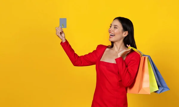 回收站概念 快乐的年轻女人拿着购物袋 看着手中的信用卡 快乐的女士享受着销售和打折 站在黄色的背景上 复制的空间 — 图库照片