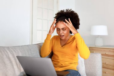 İnternet İş Mücadelesi. Bilgisayarın dokunduğu kafaya bakan umutsuz Afrikalı Amerikalı kadın dizüstü bilgisayar sorunları ve evdeki koltukta kötü internet bağlantısı yüzünden sorunlu.