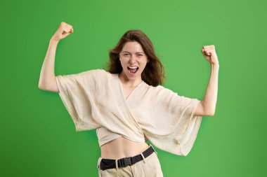 Güçlü, kendine güvenen, ağzı açık, ellerinde kasları olan, yeşil stüdyo geçmişinde izole genç bir Avrupalı bayan kazanana sevindim. Zafer duyguları, kadın gücü, spor, reklam ve teklif