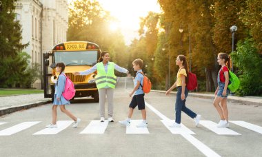 Group of children passing crosswalk on their way to school bus, diverse pupils cross the street with the crossing guard blocking traffic, boys and girls going home after classes, copy space clipart