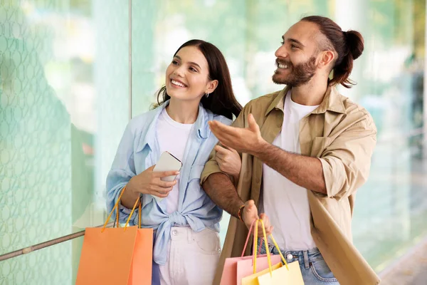快乐惊讶的年轻的欧洲男人和女人带着袋子享受购物和闲暇在一起 看看商场的橱窗 打折季节和黑色星期五的购物狂销售 — 图库照片