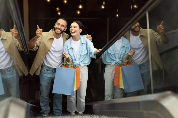 一个积极的欧洲小伙子 带着袋子拥抱女士 指指点点自由自在的空间 享受购物和逛商场的闲暇时光 销售推荐 购物狂 生活方式 爱情和关系 — 图库照片