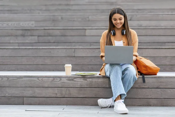 穿着时髦休闲装的快乐而美丽的年轻女性大学生 在城市地区的楼梯上工作 在户外使用笔记本电脑 喝外卖咖啡 抄袭空间 — 图库照片